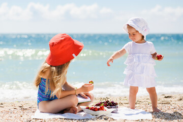 Two small sisters share food at beach