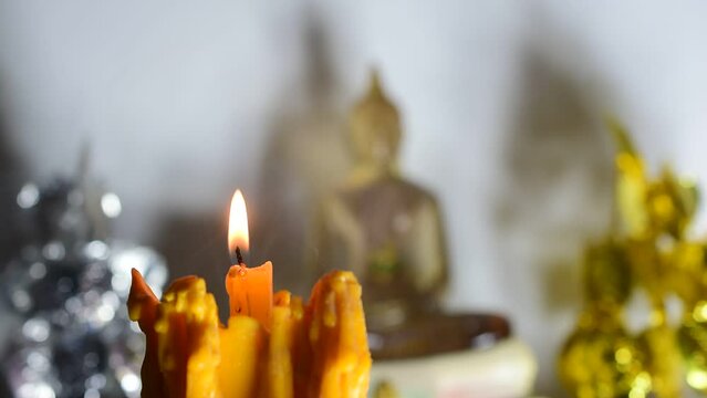 Light a candle in the temple to illuminate the golden Buddha image background.