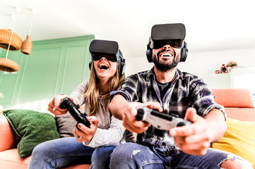 Happy young couple playing with joystick and virtual reality glasses at home couch - Smiling...