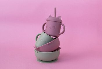 Stacked set of silicone sippy cups with straws  and bowl on pink background. Modern pastel color...
