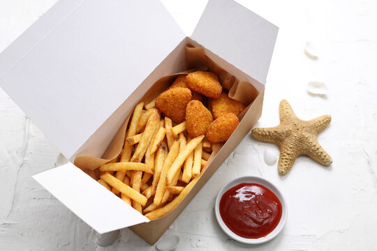 Deep fried fish nuggets in a take-away carton box and a tomato sauce, ketchup, on a white background.