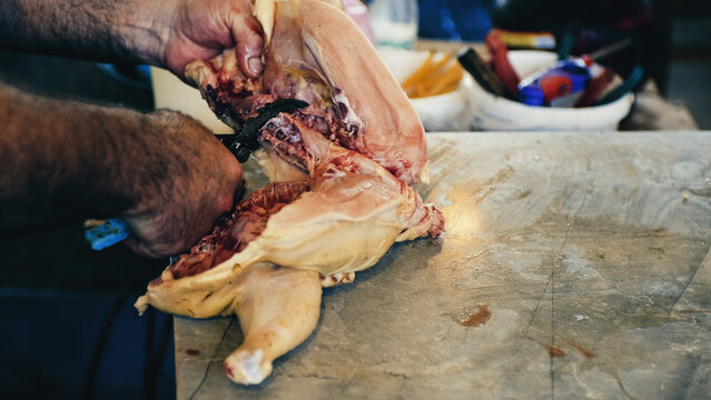 Hands of a caucasian man cutting chicken in the market. Cutting raw chicken into pieces