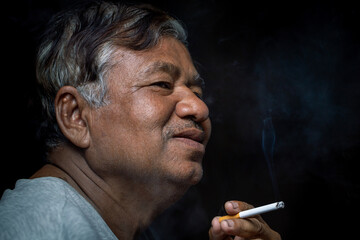 Smiling old man smoking on dark background.