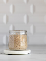 Wheat sourdough in a glass jar on a marble coaster. Ingredient for artisan bread. Copy space