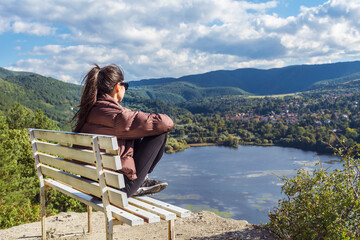 Traveler woman sitting on a bench high above a blue lake with stunning view . Scenic landscape from Bulgaria ,Pancharevo lake 