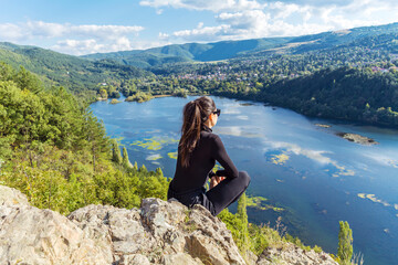 Traveler woman sitting on a rock high above a blue lake with stunning panoramic view .Traveling in the nature in Bulgaria . Pancharevo Lake