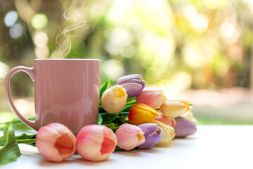 pink steaming cup of hot coffee on white wooden near window with tulip flowers and green nature...