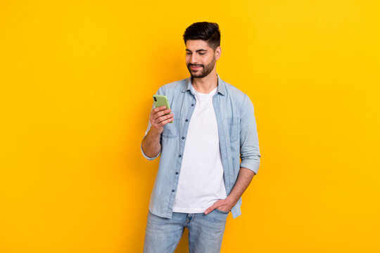 Photo of young handsome guy blogger holding phone find new content followers twitter isolated on yellow color background