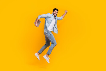 Full size photo of young guy holding laptop jump run air future technologies isolated on yellow color background