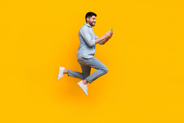 Full size photo of happy latin man blogger hold device repost comment follow wear stylish jeans outfit isolated on yellow color background