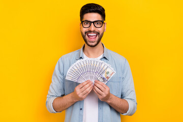 Photo of happy young guy finally got salary holding money crazy isolated on yellow color background