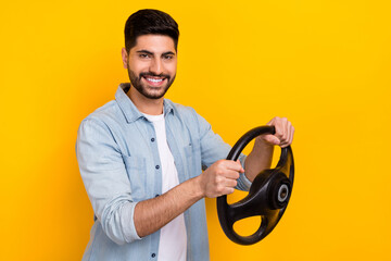 Photo of young smiling confident guy playing videogame driving car test isolated on bright yellow...