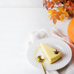 Pumpkin pie piece on plate and colored leaves on white wooden table. Halloween or Thanksgiving.