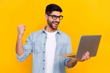 Portrait of young handsome guy holding laptop fist up celebrates good marks online education...