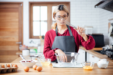 Beautiful young woman  is mixing batter, looking at camera and smiling while baking in kitchen at home ,decorating a cake of chocolate cake,cooking class, culinary, bakery, food and people concept