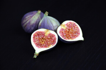 Ripe figs, half cut and whole fruits on dark wooden table	