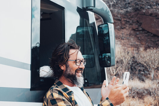 One man doing video call web using mobile phone agains a camper van vehicle. Concept of people and alternative travel vacation with motor home. Outdoor roaming connection smartphone. People tourist