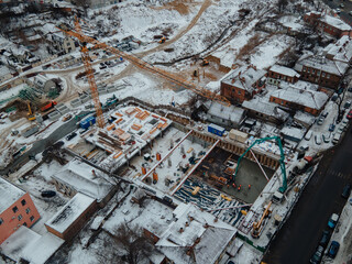 Fototapeta premium Construction of a new residential complex in winter. New housing. View of the construction site from above. Construction of a multi-storey building using a crane and concrete