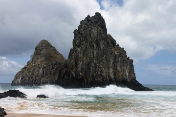 Foamy sea waves hitting sandy Cacimba do Padra beach with huge rock formations in the background
