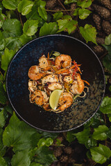 Asian cuisine. Shrimps with curry noodles. Appetizing dish on a background of leaves and plants