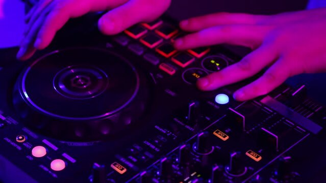 Close-up view of hands of dj maker making sounds at night club party with professional sound mixer in neon light. Modern party style. Deep beats.