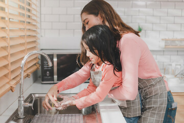 Woman helping daughter wash hands at kitchen sink. Happy young mother with daughter washing hands with liquid soap in kitchen after messy doing bakery decorating birthday cake or cooking.