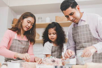 Happy family group of three diverse family, Asian and middle eastern preschool African Arab kid person make cake cooking in kitchen, Father Mother prepare decoration pretty with fun educate.