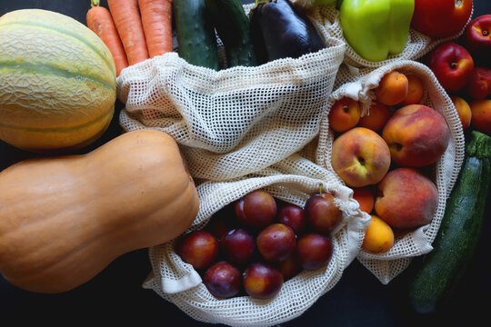Reusable mesh bags for fruits and vegetables, filled with various healthy food. Dark background, top view. - Powered by Adobe