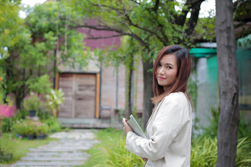 Asian businesswoman holding a tablet while smiling at the camera against a beautiful garden backdrop.