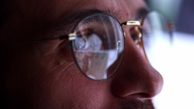 Close up view of man's eyes in eyewear looking at pc screen with computer reflection at eyeglasses. Using internet, working online, tracking database.