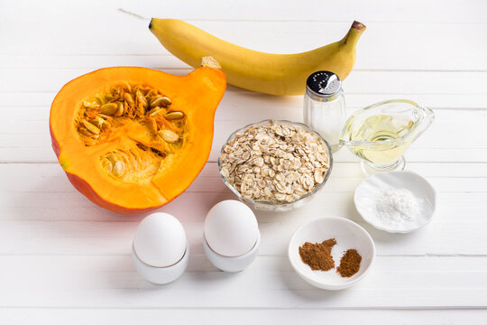 Ingredients for pumpkin pancakes with oatmeal and banana: pumpkin, banana, oatmeal, eggs, vegetable oil, spices, salt, baking powder on a white background. Cooking delicious vegetarian food.
