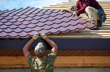 Workers install metal roofing on the wooden roof of a house. © schankz