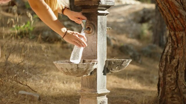A stand with drinking water taps in the forest, a girl comes up and fills a bottle.