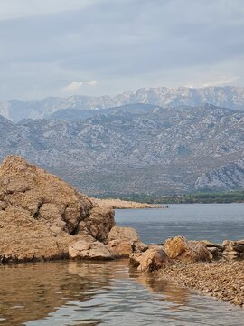 Vertical shot of rock formations in sea and rocky mountains in the background in Vinjerac, Croatia