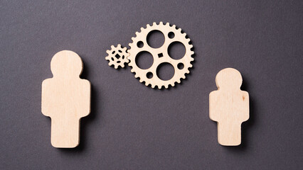 Two gears rotate between two wooden silhouettes of people Concept of teamwork