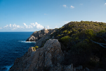 Fototapeta na wymiar The lighthouse of Cala Ratjada. Waves splashing on a rocky coastline of Mallorca in the mediterranean sea. Deep blue water and steep cliffs. 