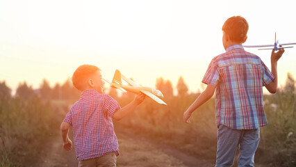 Siblings run past wheat fields to launch bright toy airplanes. Couple of excited brothers enjoys spending summer holidays together in countryside, sunlight