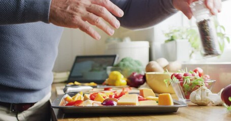 Midsection of caucasian man standing in kitchen, cooking dinner, seasoning food