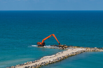 An excavator and a mining truck move stones into the sea. Construction of breakwaters to protect...