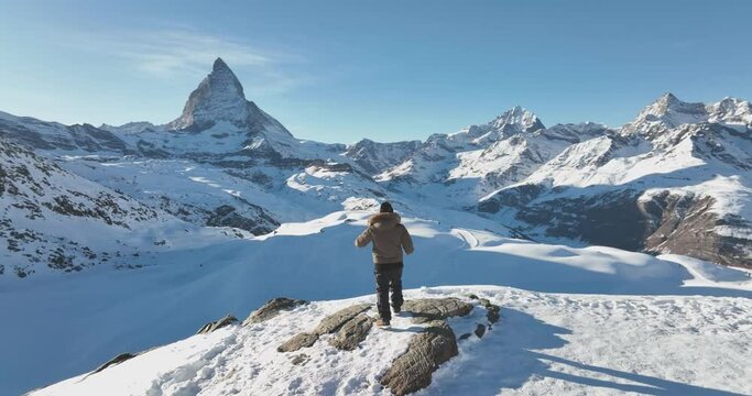 Successful asian man celebrate and raising arms on mountain peak view point with iconic famous Matterhorn background. Swiss alps, Switzerland. Travel and Adventure concept. Aerial drone orbit shot.