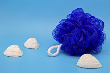 Blue mesh pouf bath sponge washcloth with sea shells on blue background closeup photo with copy space. Soft synthetic shower wash cloth. Washing hygiene design element. Spa body care accessory product