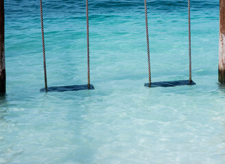 Two empty swings on the water by the sea at a tropical beach. Vacation travel concept