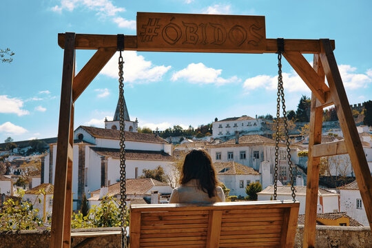Chica sentada en un columpio ante la panom&aacute;rica de la ciudad de &Oacute;bidos en Portugal