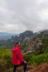Fototapeta na wymiar Woman with scenic view of Holy Monastery of Rousanos and Holy Monastery St Nicholas Anapafsas appearing from fog, Kalambaka, Meteora, Thessaly, Greece, Europe. Misty atmosphere in dramatic landscape