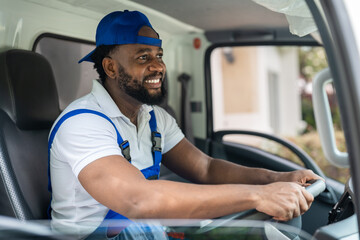 Smiling professional man mover worker in blue uniform driving truck to delivery and moving house...