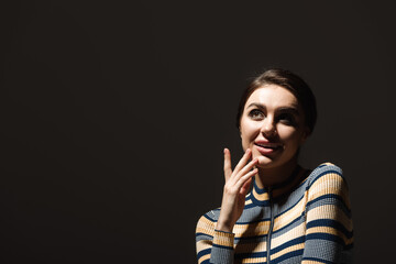 pleased young woman in striped turtleneck looking away isolated on black.