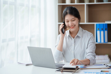 Charming and smiling Asian business woman Talk to customers on mobile phones and use their laptops to do office work.