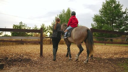 riding coach is training future champion in pony club, little boy is riding horse at first time