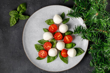 Caprese salad in the form of a Christmas tree. Festive tomato mozzarella and basil appetizer on light plate.