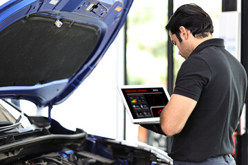 Car mechanic working with a laptop in Auto Repair Service checking car engine	